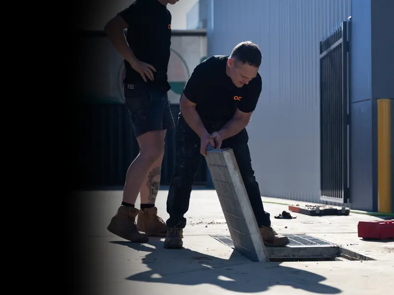 Two Central Vic Jetting technicians lifting a drain grate on a job site